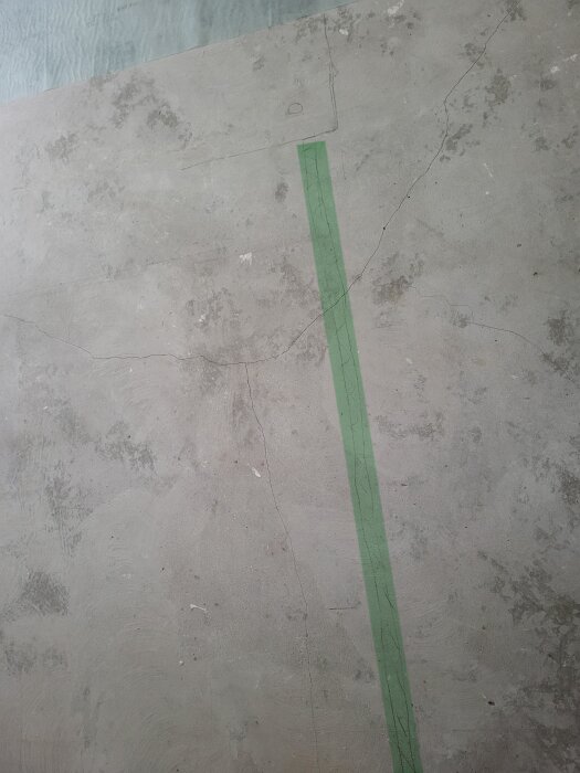 Betonggolv med en grön tejplinje och flera sprickor, där det planeras att fräsas för att gömma en elkabel.