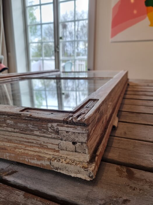 Gammalt fönster med avskrapad färg, eventuella rötskador synliga längs nederkanten av bågen på ett träbord.