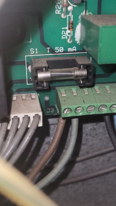 En närbild av ett kretskort med en glas säkring, några kablar och olika elektroniska komponenter.