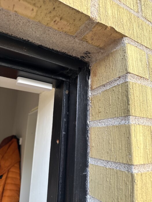 Gul tegelvägg och dörrkarm med svarta och vita detaljer, sedd från en öppen dörr inåt mot en hall.