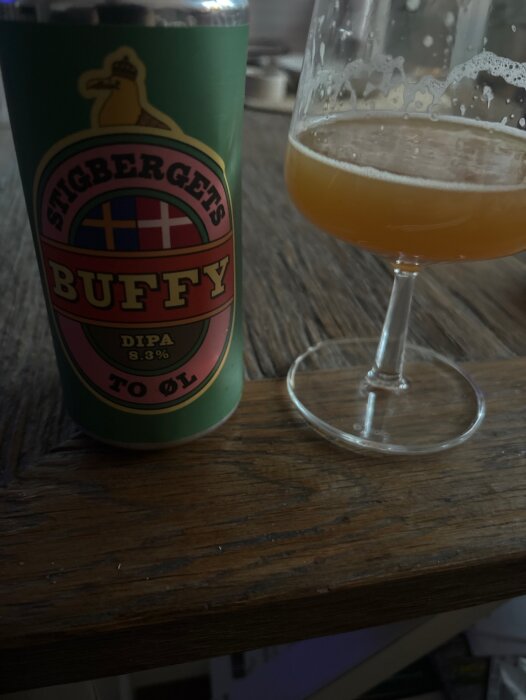 En burk Stigbergets Buffy DIPA 8.3% står bredvid ett halvtomt glas med öl på ett träbord.