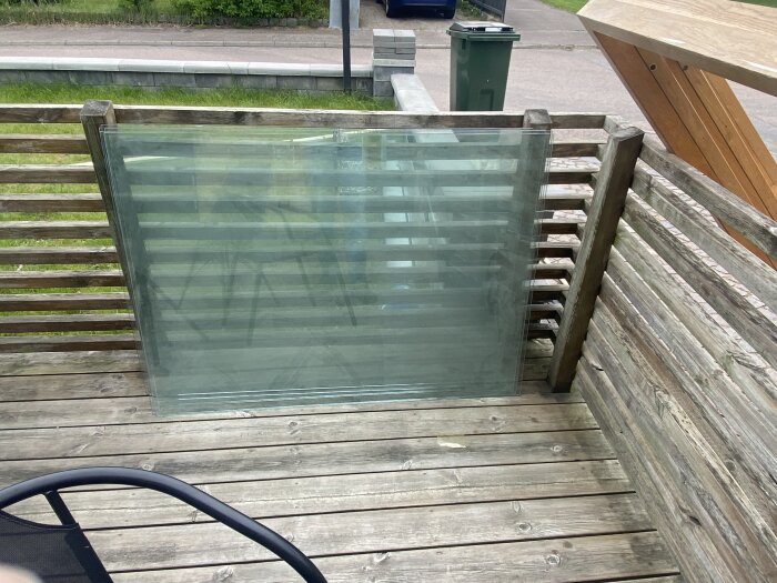 Stort glas lutat mot en trästaket på en terrass med plankgolv i en trädgårdsmiljö.