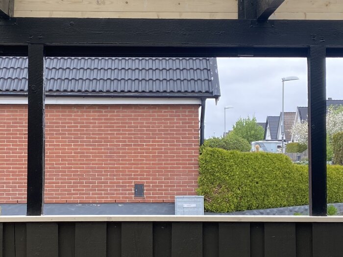 Öppen fönsterram i en carport, sedd utåt mot en tegelvägg och grönskande häck; diskussion om hur ett större glas kan monteras här.