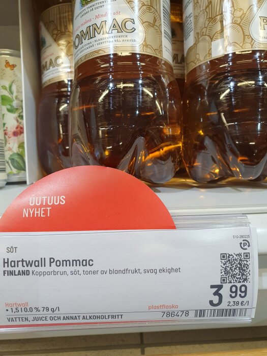 Flaskor med Hartwall Pommac i butikshylla med prisskylt, kopparbrun färg, beskrivs som söt med toner av blandfrukt.