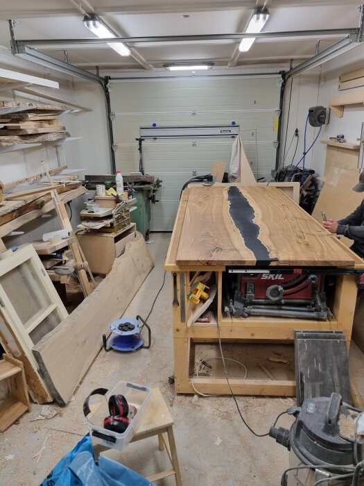 Verkstad med epoxibord under arbete, omgiven av verktyg och träplankor. Bordet har träfinish och pågående epoxilager.