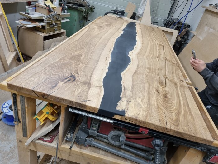 Epoxibord med mittendelen i svart, omringat av trästruktur, delvis behandlat med finish. Synlig arbetsbänk och hantverkare i bakgrunden.