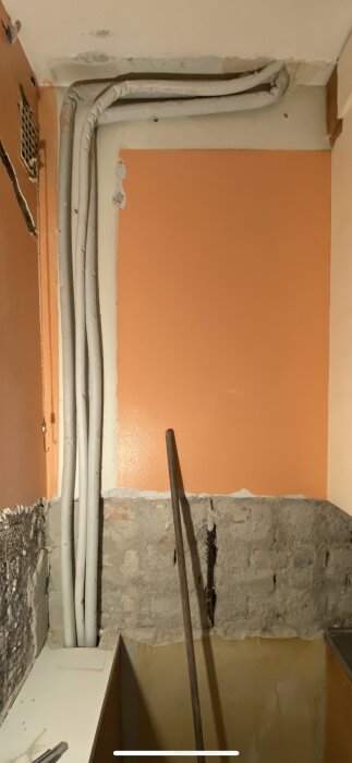 Vägg med synliga rör och ofärdigt murverk i en pågående renovering; väggen målad i orange.