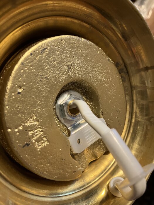 Närbild av en bordslampas undersida med en fast mutter på en gängstång och en vit kabel i fokus.