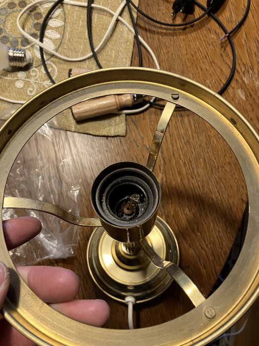 Guldfärgad bordslampa sedd underifrån med fokus på gängstång och mutter; lampfot och elektriska komponenter synliga.