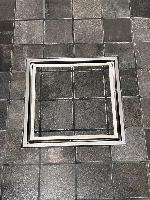 Grå klinkergolv med en fyrkantig klämring centrerad, där mindre rutor omger den större, täcker hela och ligger kant i kant.