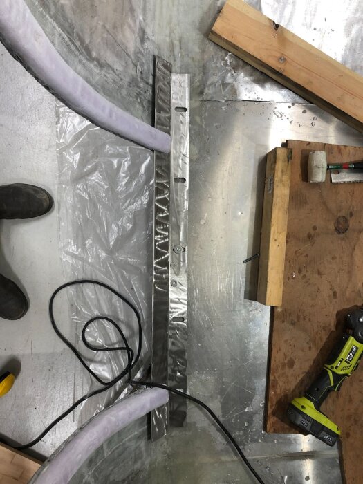 Verkstadsgolv med bockad rostfri plåt använd som tröskel, omgiven av verktyg, träbit, kabel och polyuretanskum i ett byggprojekt.