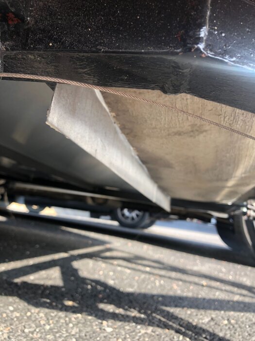 Undersida av släpvagn med rostfri tröskel i 3mm plåt som är fastbultad och plastad med glasfiber, sett med skugga på marken.