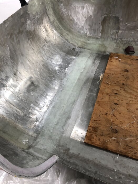Ett äggskalsformigt underrede med plastad yta och en rostfri tröskel av stålplåt, delvis täckt av träskiva och omgiven av glasfiber.