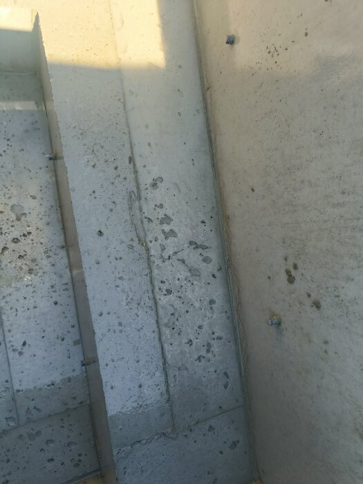 Nygjuten betongform med gropar och ojämnheter på ytan, blottade skruvar syns på höger sida, tre bänkformade element.
