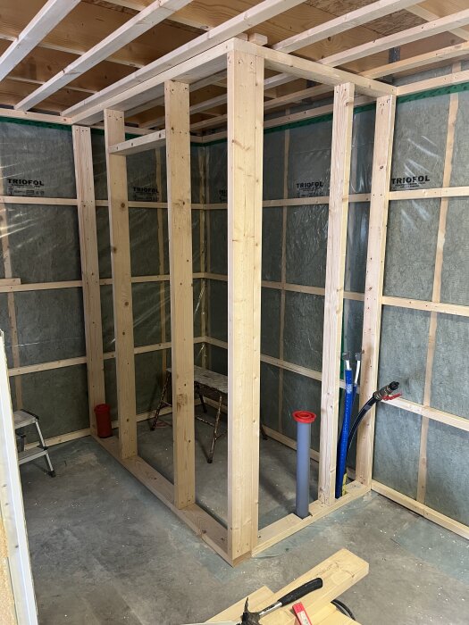 Träram för en framtida toalett med gipsskivor i bakgrunden och byggutrustning på golvet.