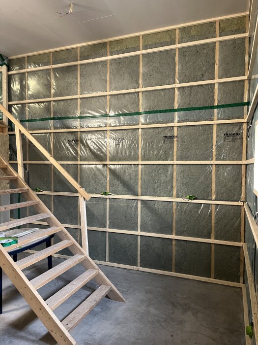 Råvägg med träreglar och isolering, nyligen dragna elkablar, trappa leder uppåt. Förberett för att sätta gipsväggar och framtida toalett.