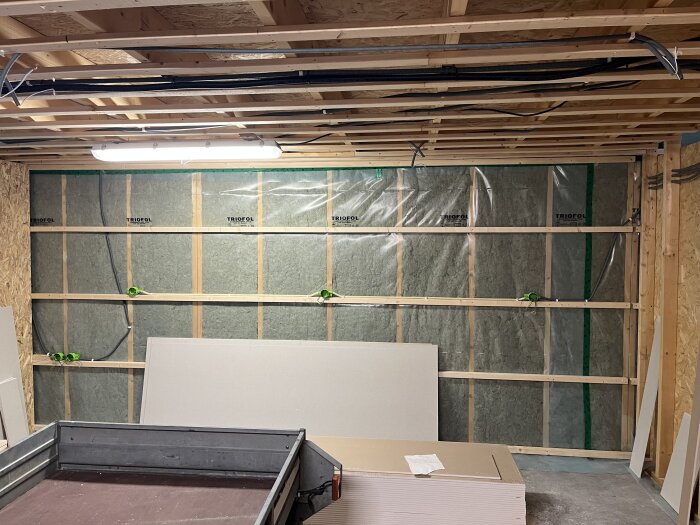 Byggarbetsplats med isolerad vägg, gipsplattor och synliga kablar i taket, förberett för installation i ett hemmarenoveringsprojekt.