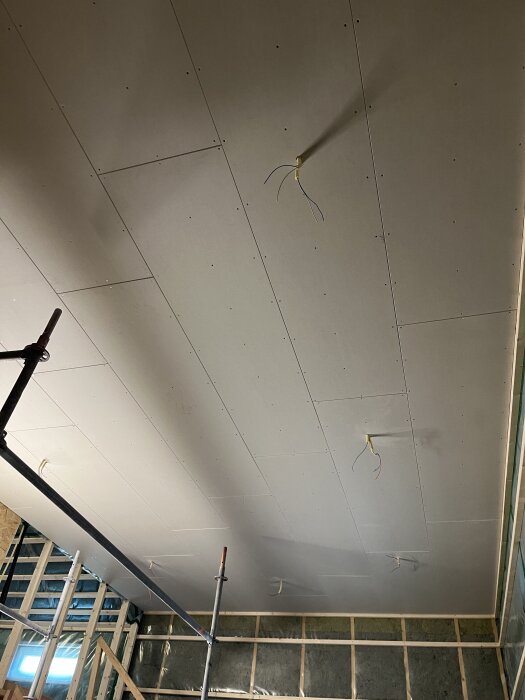 Gipstak med synliga elkablar och ställning i ett rum under renovering.