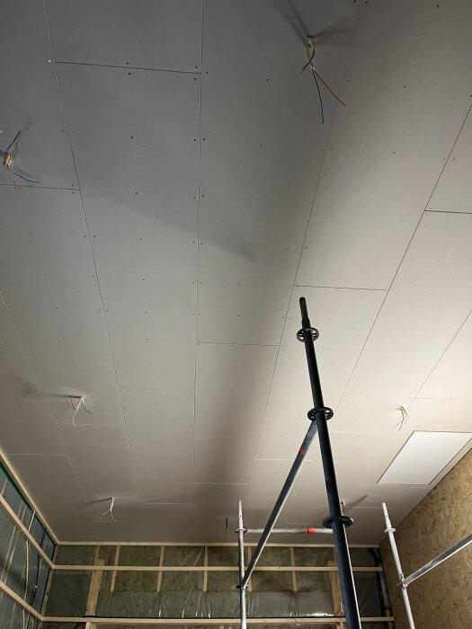 Gipstak med installerad el, sett från en byggarbetsplats med ställning i förgrunden och synliga elkablar från taket.