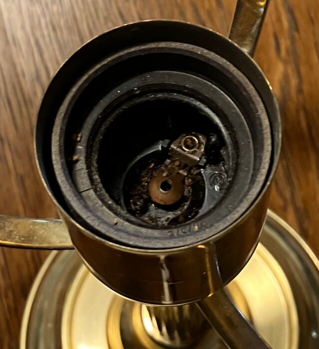 Närbild av en lampfot inuti med synlig metallkontakt och skruv, saknar glödlampa. Mörk interiör mot en träyta i bakgrunden.