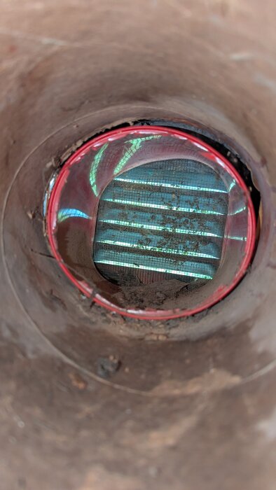 Ventilationsrör sett från insidan, visar ett papprör med ett insatt plast rör och metallgaller i bakgrunden förhindrar kallras och förbättrar ventilation.