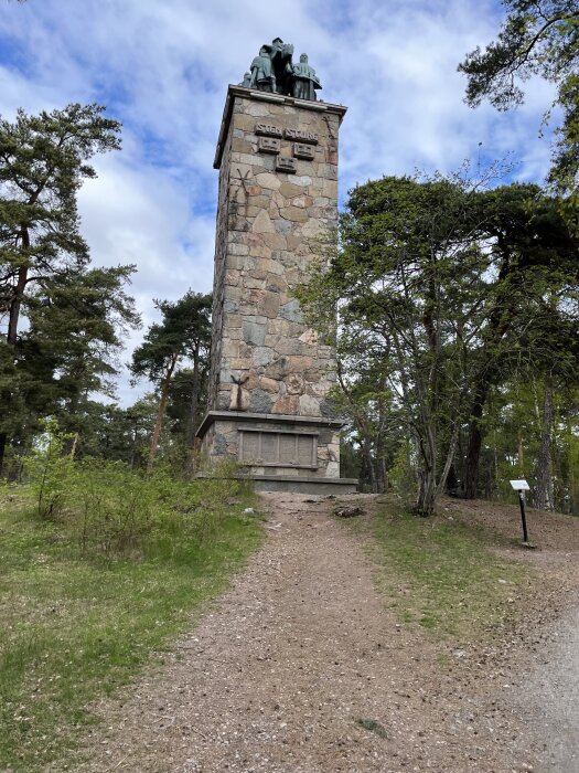 Minnesmonument av sten i skogsmiljö, med statygrupp och texten "Sten Sture" ingraverad högst upp. Stig leder fram till monumentet.