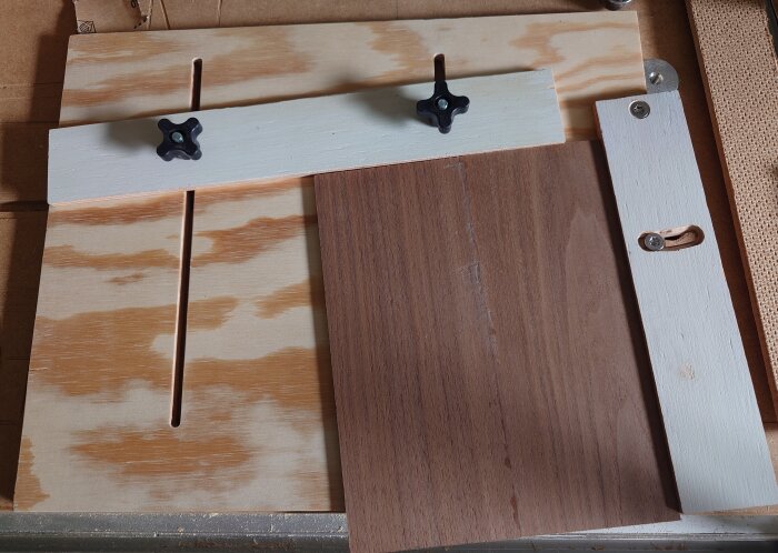 Träjigg med stjärnskruvar och träbit monterad på plywoodskiva för kantfräsning och justering vid byggprojekt.