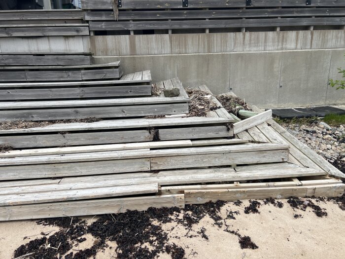 Trätrappa från altan ner till stranden, delvis sönder och täckt av sand och tång efter stormar, visar behov av stabilare konstruktion.