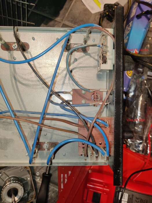 Elektrisk anslutning inuti en byggfläkt med blå och bruna kablar kopplade till ett kretskort nära vred för fläkthastighet.