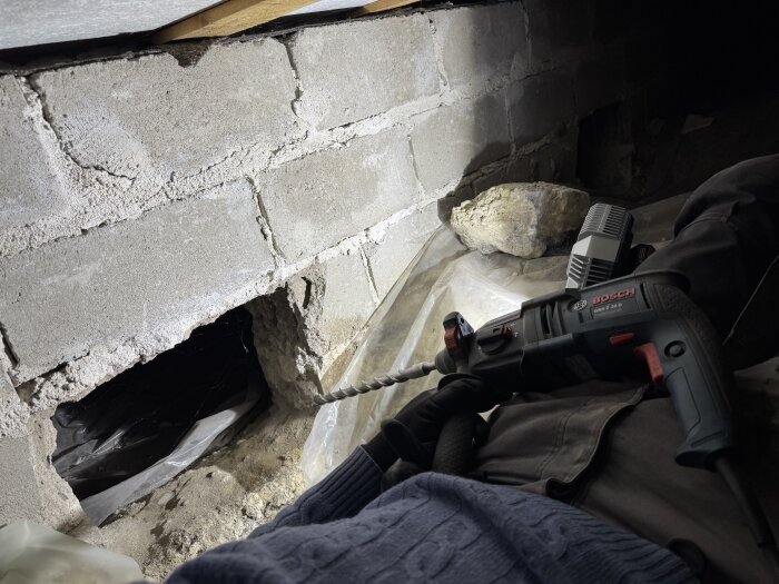 Person borrar i en krypgrund med en Bosch borrmaskin, förbereder för installation av vägguttag.