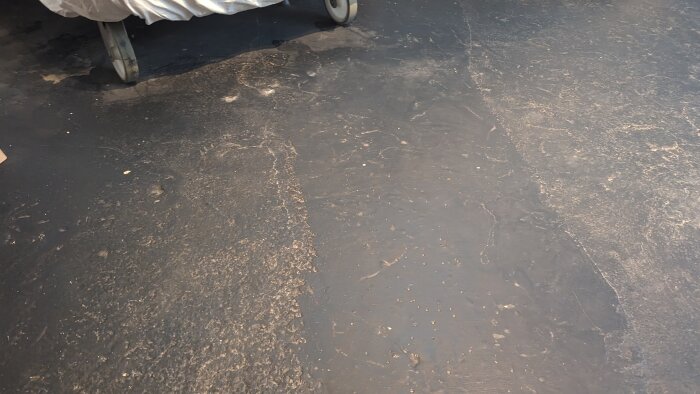 Slitet betonggolv i oinredd källare med gammal yta och hjul från en möbel i övre vänstra hörnet.