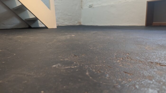 Oinrett källargolv med ojämn yta, en del av en trappa syns. Potentiellt renoveringsprojekt för gästrum eller kontor.