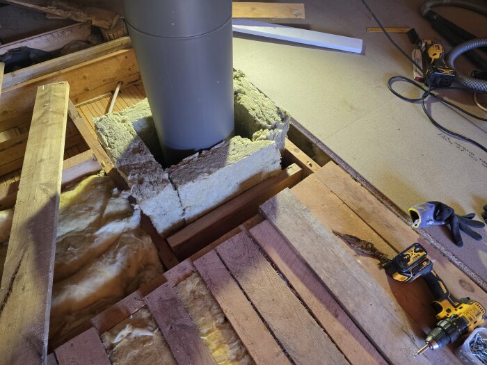 Kaminrör genom golv med synlig isolering och verktyg liggande på träskivor. Golvspånskivor synliga i bakgrunden.