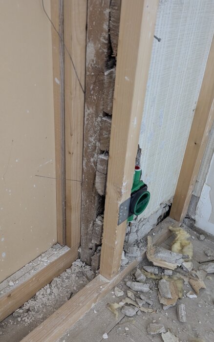 Vägg av träreglar och gips i en gammal lägenhet. Puts och skräp på golvet, visar delar av väggstruktur från renovering.