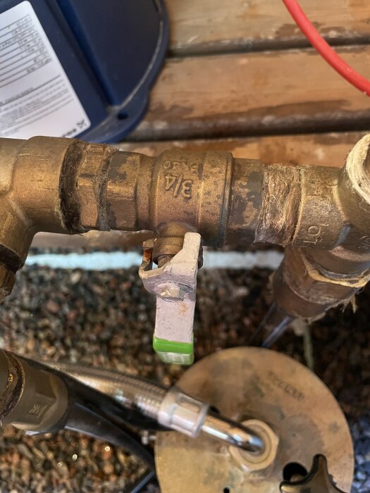 Kulventil med grönt vred och rostiga delar, omgiven av gängade rörkopplingar.