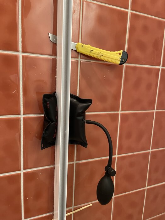 Pumppåse och gul kniv används för att demontera del på kaklad vägg.