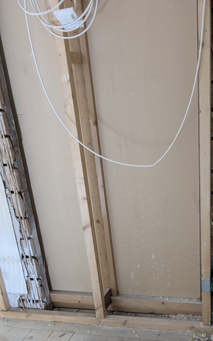 Gipsvägg med synliga träreglar och elkablar, delvis borttagen puts och vassmatta till vänster.