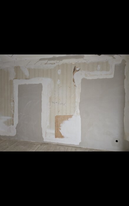 Sliten vägg med spår av tidigare lagningar och borttagna dörröppningar, delvis täckt med tapet och gips, synlig vassmatta och puts.