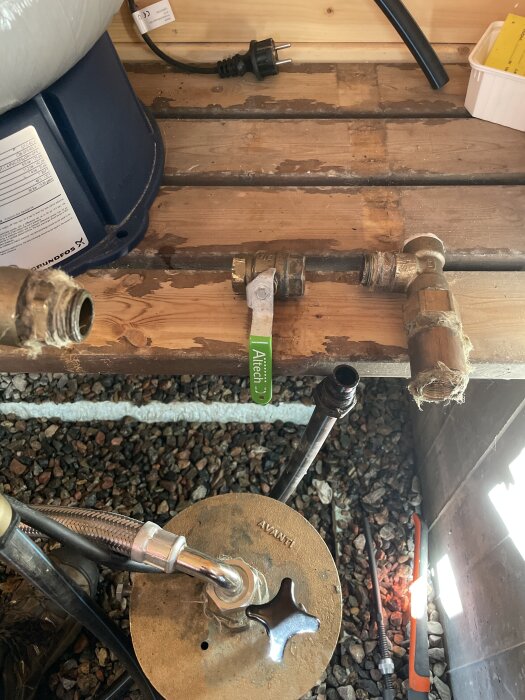 Rörledningar och kopplingar på en träyta med verktyg, inklusive en grön rörtång och svart sladd. Fråga om att täta gängor.