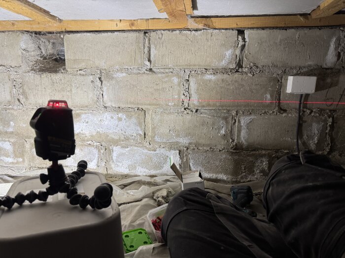 Laserverktyg används för att justera en kabel i krypgrund, sladdar syns på vägg och verktyg ligger på marken.