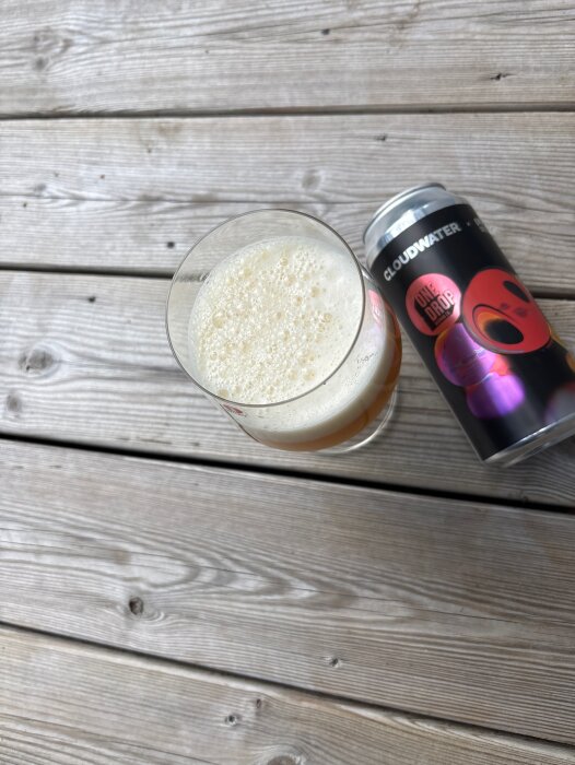 Ölglas med skummigt innehåll bredvid en One Drop-burk från Cloudwater, placerad på ett träbord.