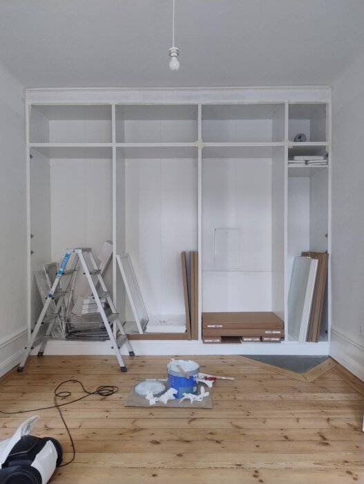 Omonterade garderober på plats, stege bredvid, byggmaterial och färg på trägolv. Inbyggd design med hålkälslist ovan planeras.