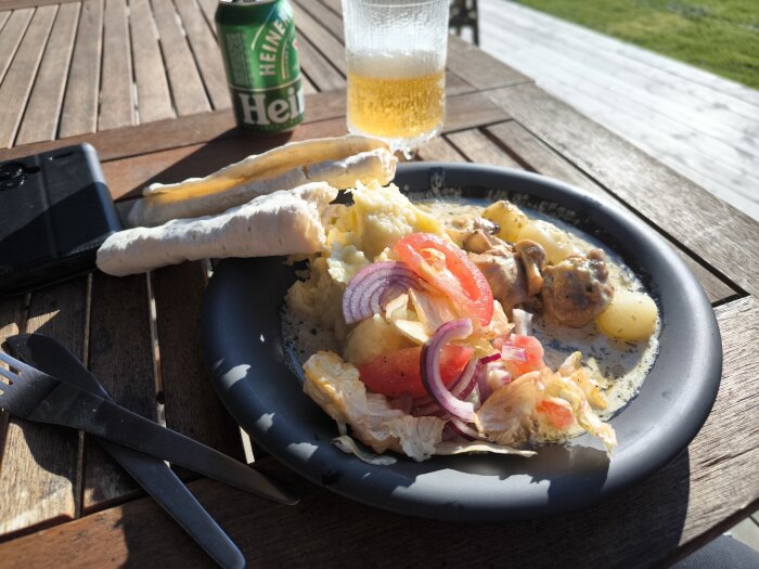 Tallrik med dragonkyckling, hemlagat mos och sallad på träbord utomhus, bredvid ölburk och glas.