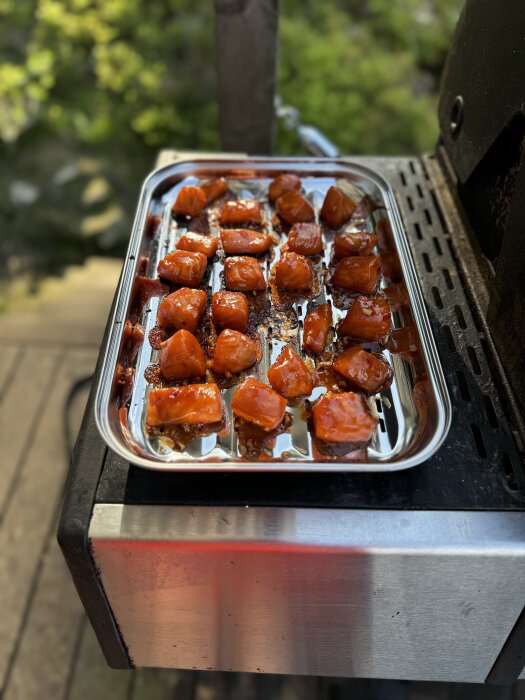 Egenrökta laxbitar på ett grillgaller, marinerade och varmrökta efter gravning över natten, ligger färdiga på en rostfri plåt på grillen.