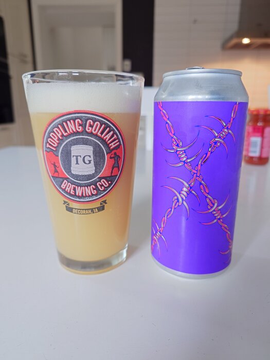 Ett glas med öl från Toppling Goliath Brewing Co. och en färgglad burk med mönster, stående på ett köksbord.