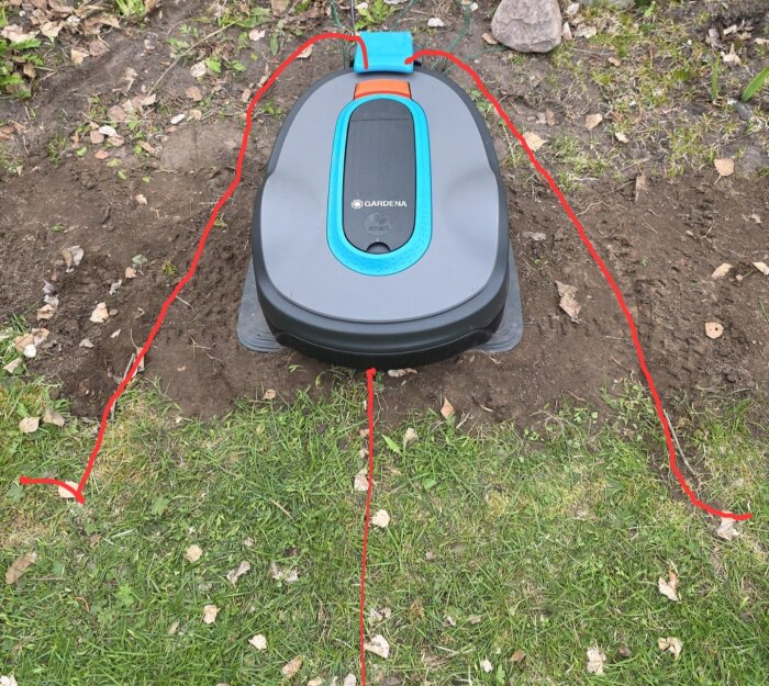 Robotgräsklippare vid laddstation med synliga avgränsningskablar på gräs.