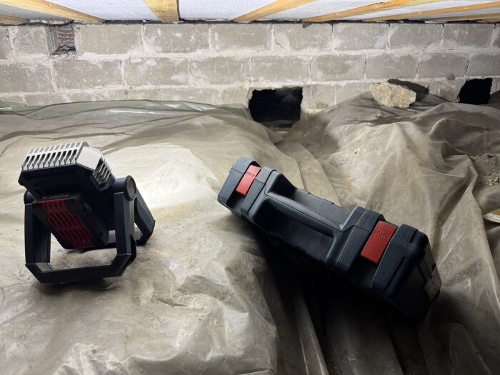 Bosch 18V led-lampa och väska på plastskyddad betonggolv under byggprojekt.