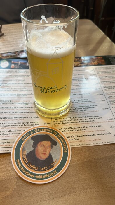 Ett glas öl från Brauhaus Wittenberg på ett bord med en meny och en ölunderlägg med Martin Luthers porträtt.