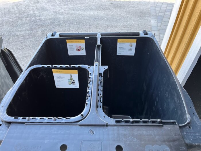 Öppen soptunna med två fack för återvinning, ett för färgat glas och ett för plast-/pappersförpackningar i Södertälje kommun.