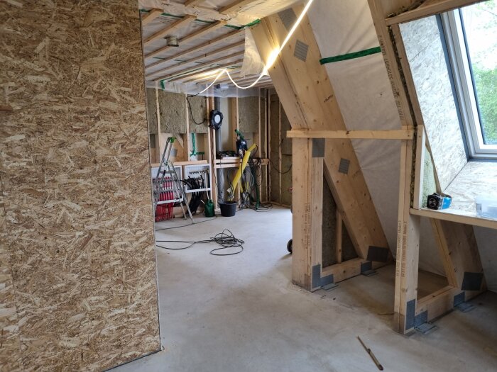 Renoveringsprojekt med isolering, träreglar och snedtak. Stege och verktyg syns i bakgrunden, samt fönster mot framsidan.